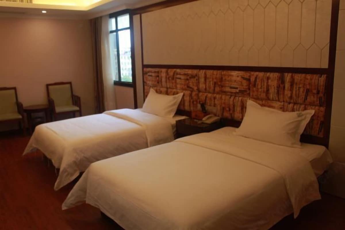 Quarto de hotel com duas camas de solteiro, mesa de cabeceira, uma cadeira e uma janela.