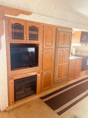 Una cocina con armarios de madera, estufa empotrada y televisor.