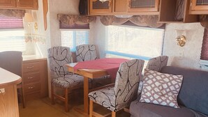 A compact RV interior with a dining table, two chairs, a sofa, and wooden cabinets.