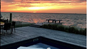 Vista del atardecer desde una zona de piscina con muelle de madera, una silla de descanso y un banco.
