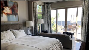 Un hotel moderno con una cama grande, un sofá, un escritorio y vista al mar a través de puertas de vidrio.