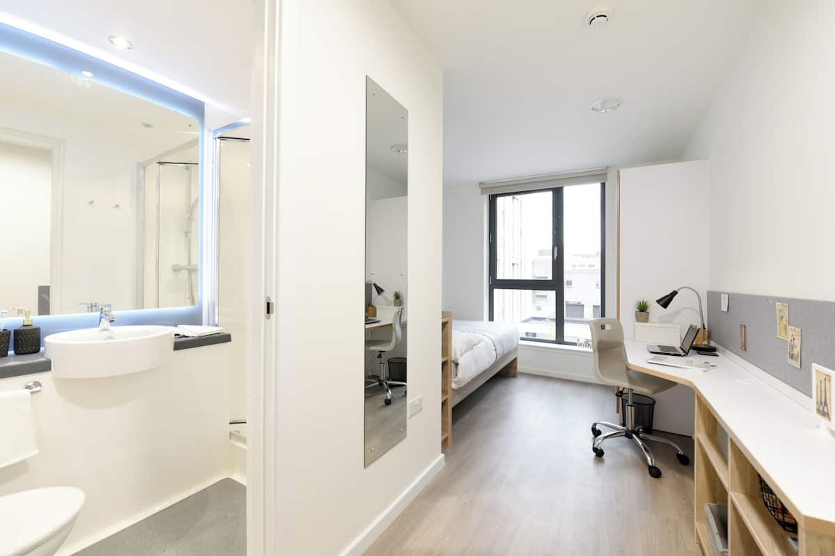 A modern hotel room with a bathroom, a bed, a desk, and a large window.