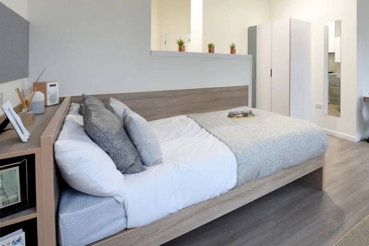 A modern bedroom with a bed, a bedside table with a radio, and a mirror above the bed.