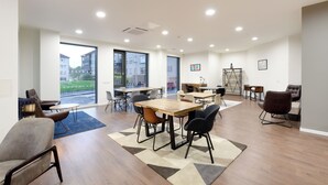 A spacious indoor area with multiple tables and chairs, large windows, and a view of buildings outside. - For Students Only Bright Ensuite at St Mungo's in Glasgow (Glasgow)