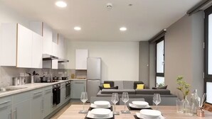 A modern kitchen with grey cabinets, a dining table set with plates and glasses, and a grey sofa in the background. - For Students Only Bright Ensuite at St Mungo's in Glasgow (Glasgow)
