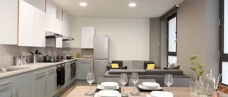 A modern kitchen with grey cabinets, a dining table set with plates and glasses, and a grey sofa in the background.