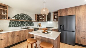 Une cuisine moderne avec des meubles en bois, un réfrigérateur noir et un plan de travail blanc.