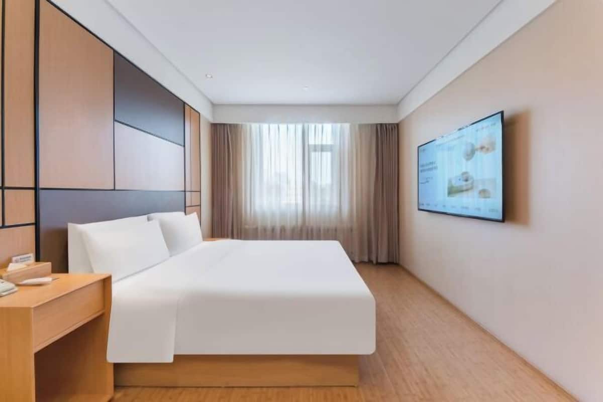 Ein Hotelzimmer mit Bett, Schreibtisch, Fernseher und einem Fenster mit Vorhängen.