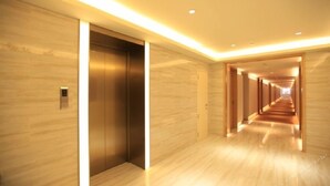 Un pasillo moderno de hotel con suelo y paredes de madera, que incluye un ascensor y un largo pasillo con puertas a ambos lados.