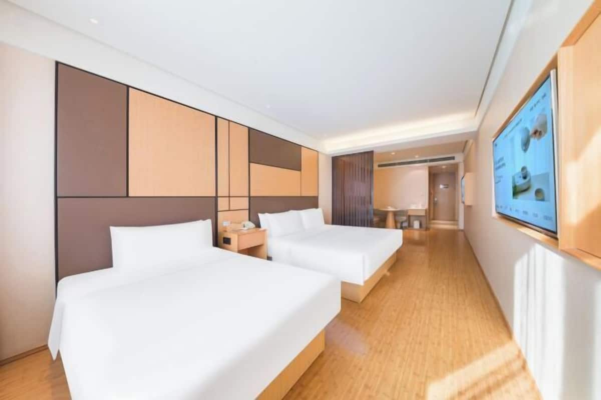 Ein Hotelzimmer mit zwei Betten, einem Fernseher an der Wand und Holzboden.