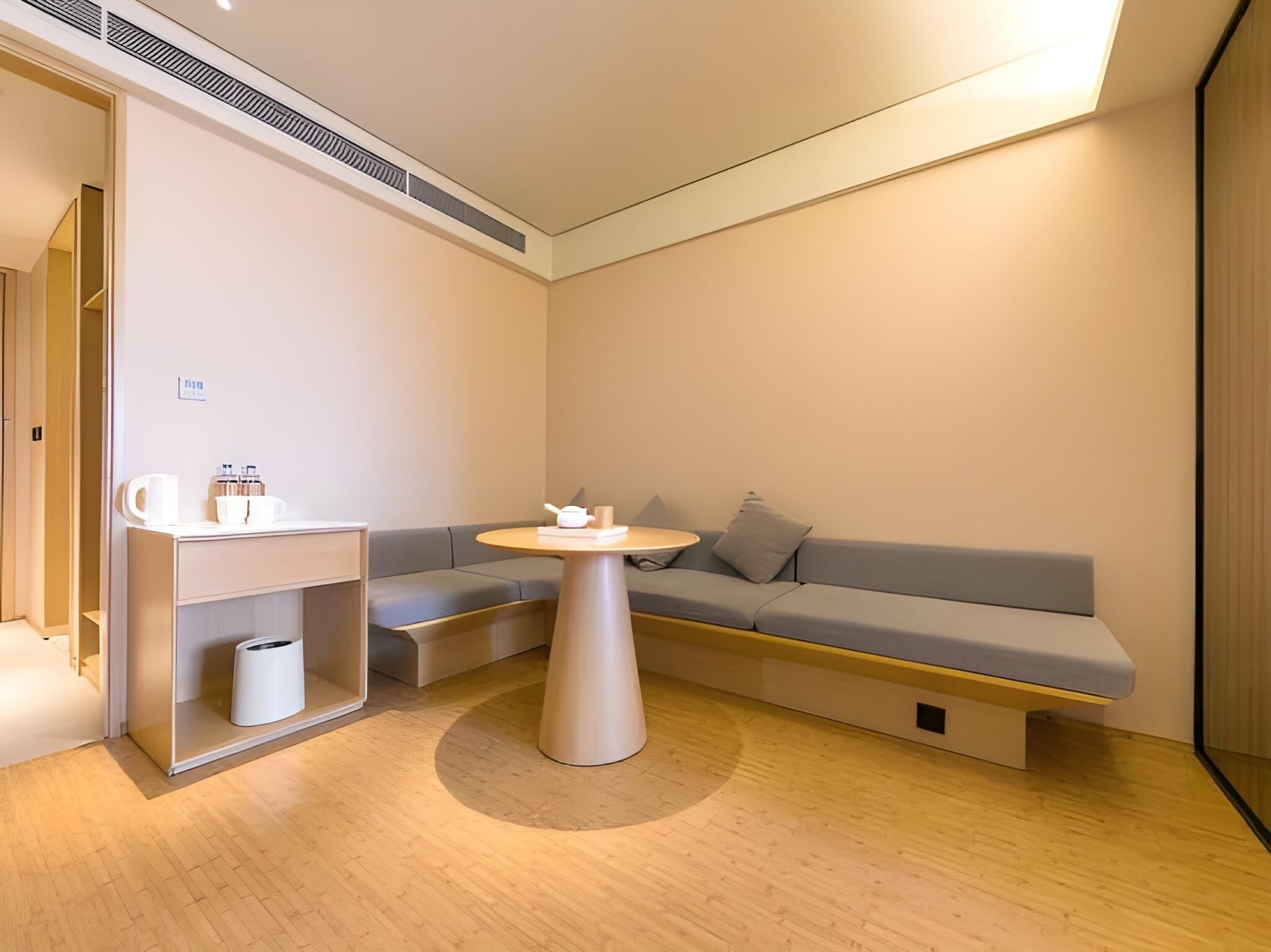 Et moderne, minimalistisk værelse med en grå sofa, et lille rundt bord og en indbygget hylde med toiletartikler.