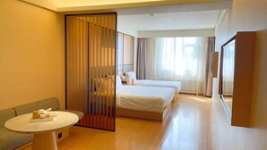 Una habitación de hotel con un sofá, una mesa redonda, dos camas y un amplio ventanal con cortinas.