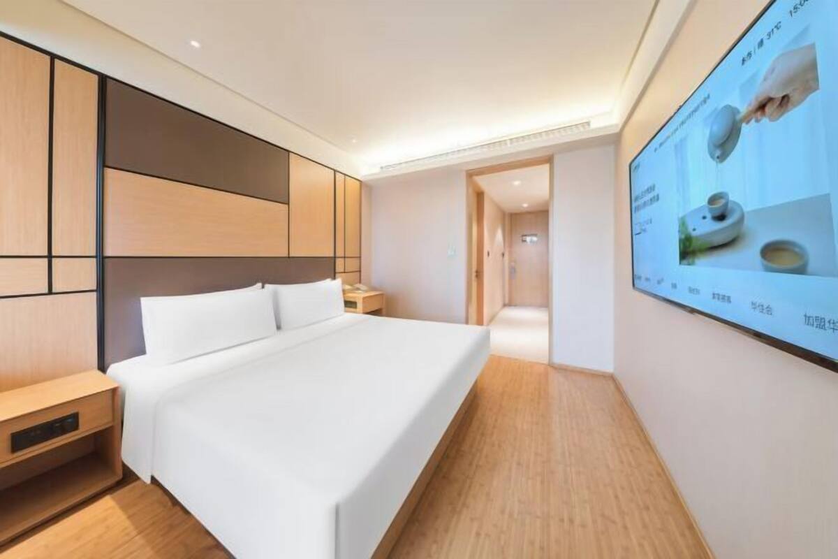 Ein modernes Hotelzimmer mit einem großen Bett, Nachttischen, einem an der Wand befestigten Fernseher und Holzboden.