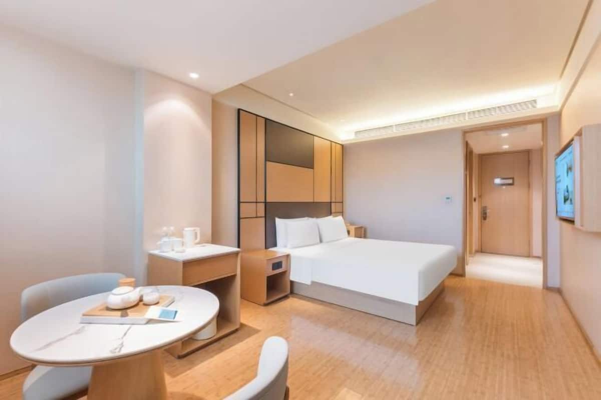 Ein modernes Hotelzimmer mit einem Bett, Nachttisch, Stuhl und einem kleinen runden Tisch mit einem Buch und einer Teekanne.