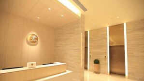 Un área de recepción de hotel moderna con un mostrador de madera, un logotipo en la pared y una planta en maceta.