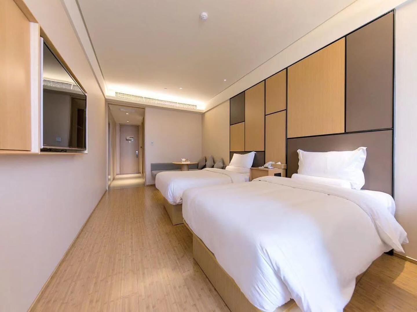 A modern hotel room with two beds, a large mirror, and a wooden floor.