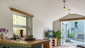A kitchen with a wooden island, a dining area with a sofa, and a view of a stone building outside. - 1 bedroom accommodation in Buxton (Buxton)