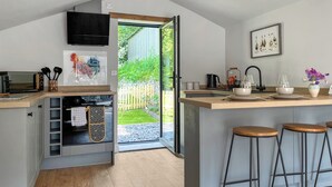 A modern kitchen with a large island, bar stools, a TV, and a view of a garden through a glass door. - 1 bedroom accommodation in Buxton (Buxton)