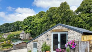 A stone cottage with a small porch, a wooden fence, and potted plants. - 1 bedroom accommodation in Buxton (Buxton)