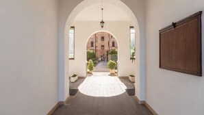 A hallway with an arched ceiling, a hanging light fixture, and a view of a courtyard with a building in the background. - DELUXE Suite, stunning view of the Tiber River. Top floor with elevator (Roma)