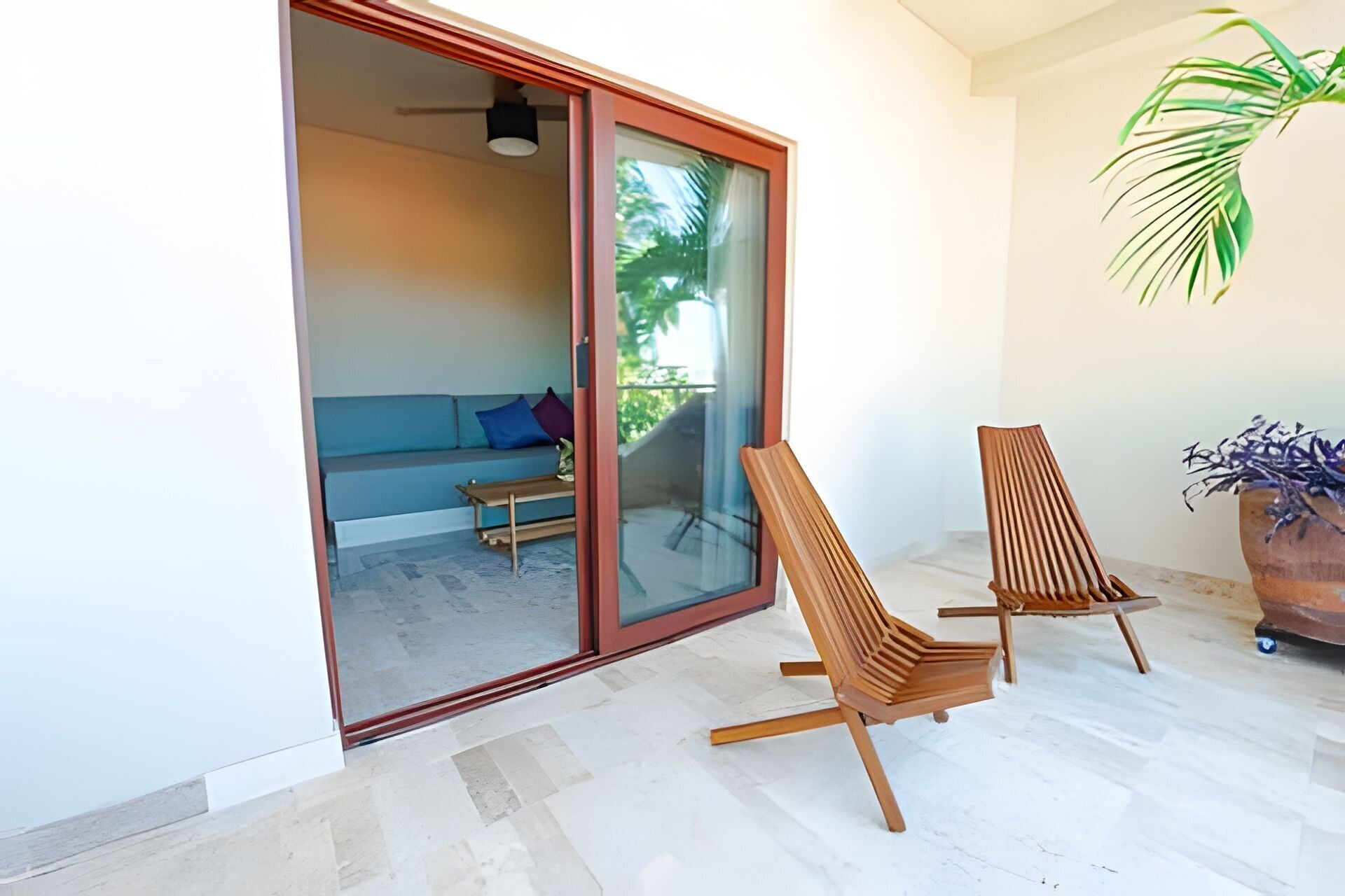 Un balcon avec une porte-fenêtre coulissante, un canapé, deux chaises en bois et une plante en pot.