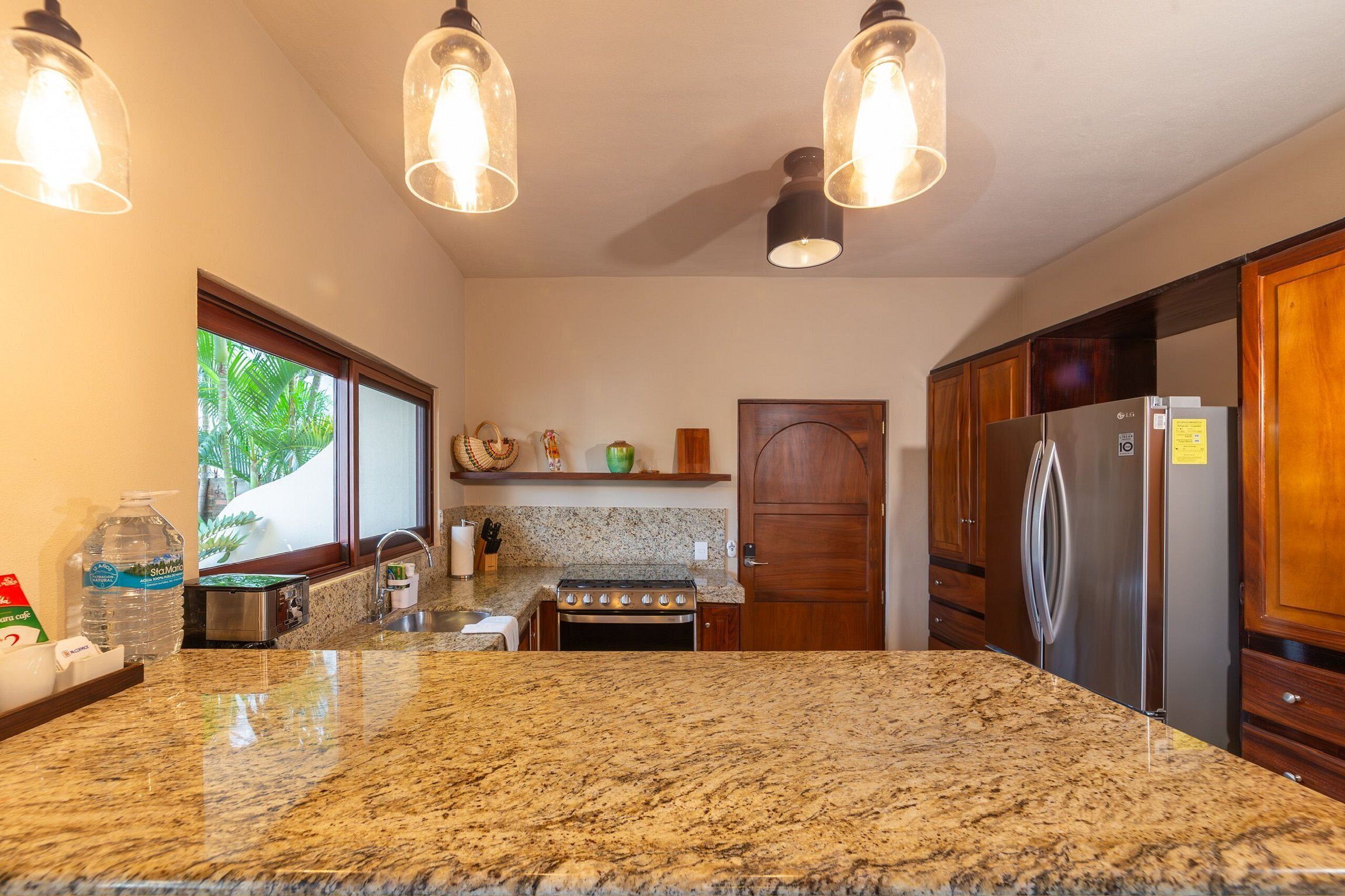 A kitchen with granite countertops, stainless steel appliances, wooden cabinets, and pendant lighting.