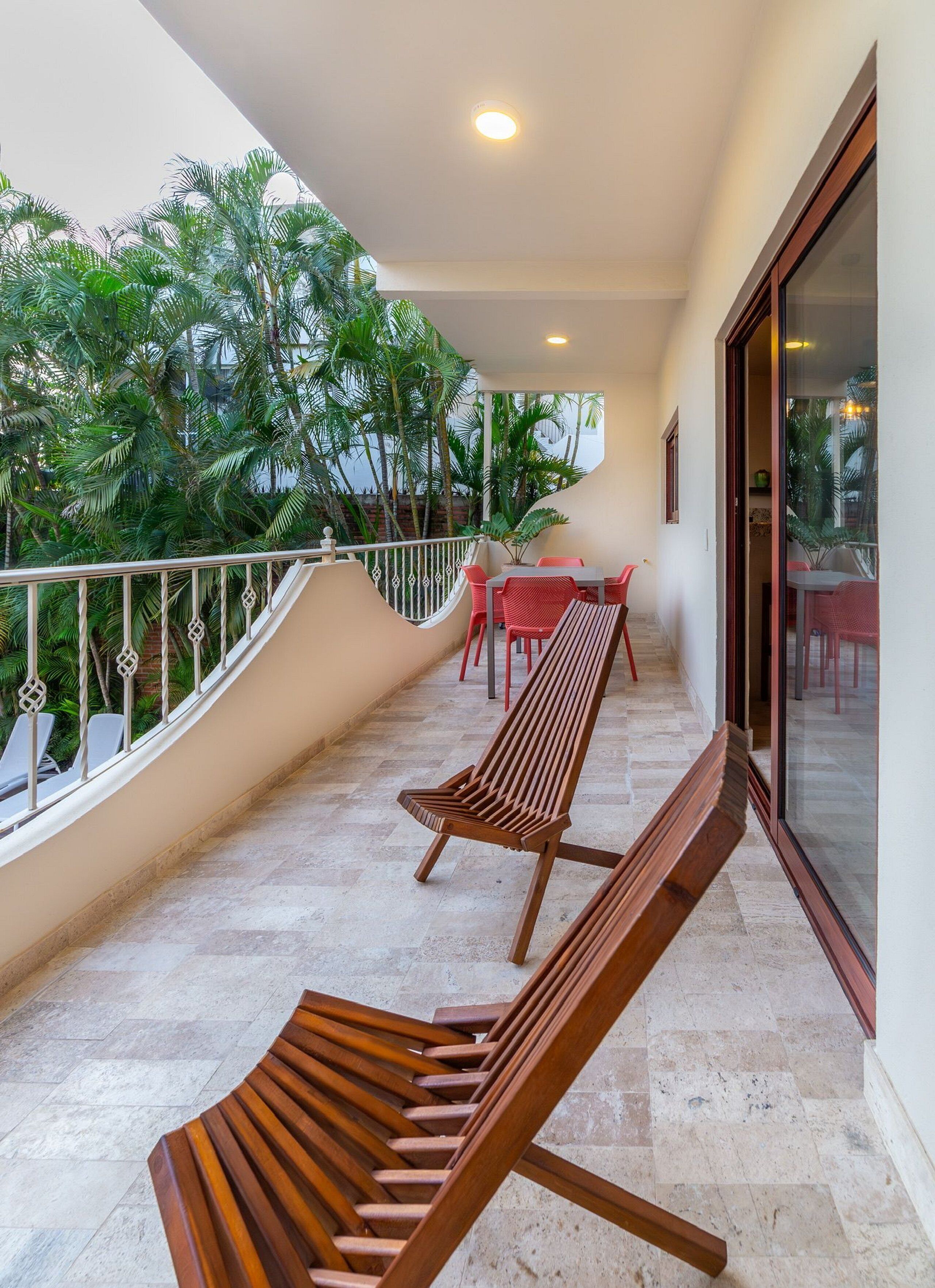 A balcony with a wooden bench, a table with chairs, and a view of lush green trees.