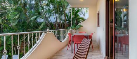 A balcony with a wooden bench, a table with chairs, and a view of lush green trees.