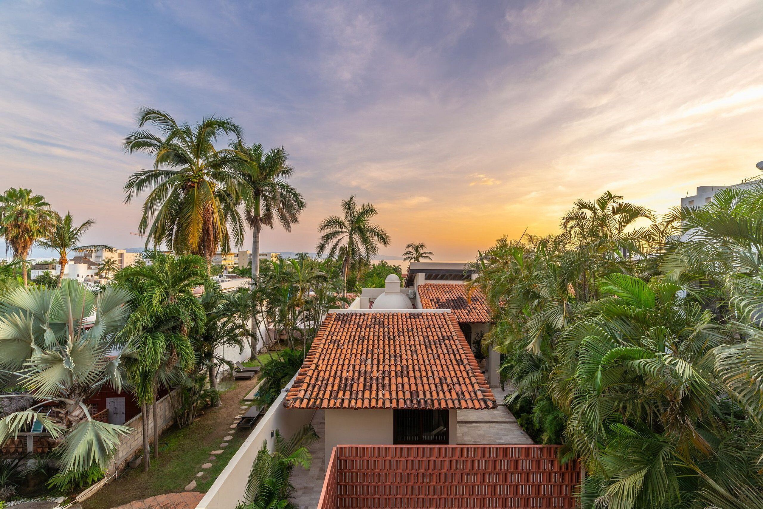 A residential area with terracotta-tiled roofs, palm trees, and a clear sky.
