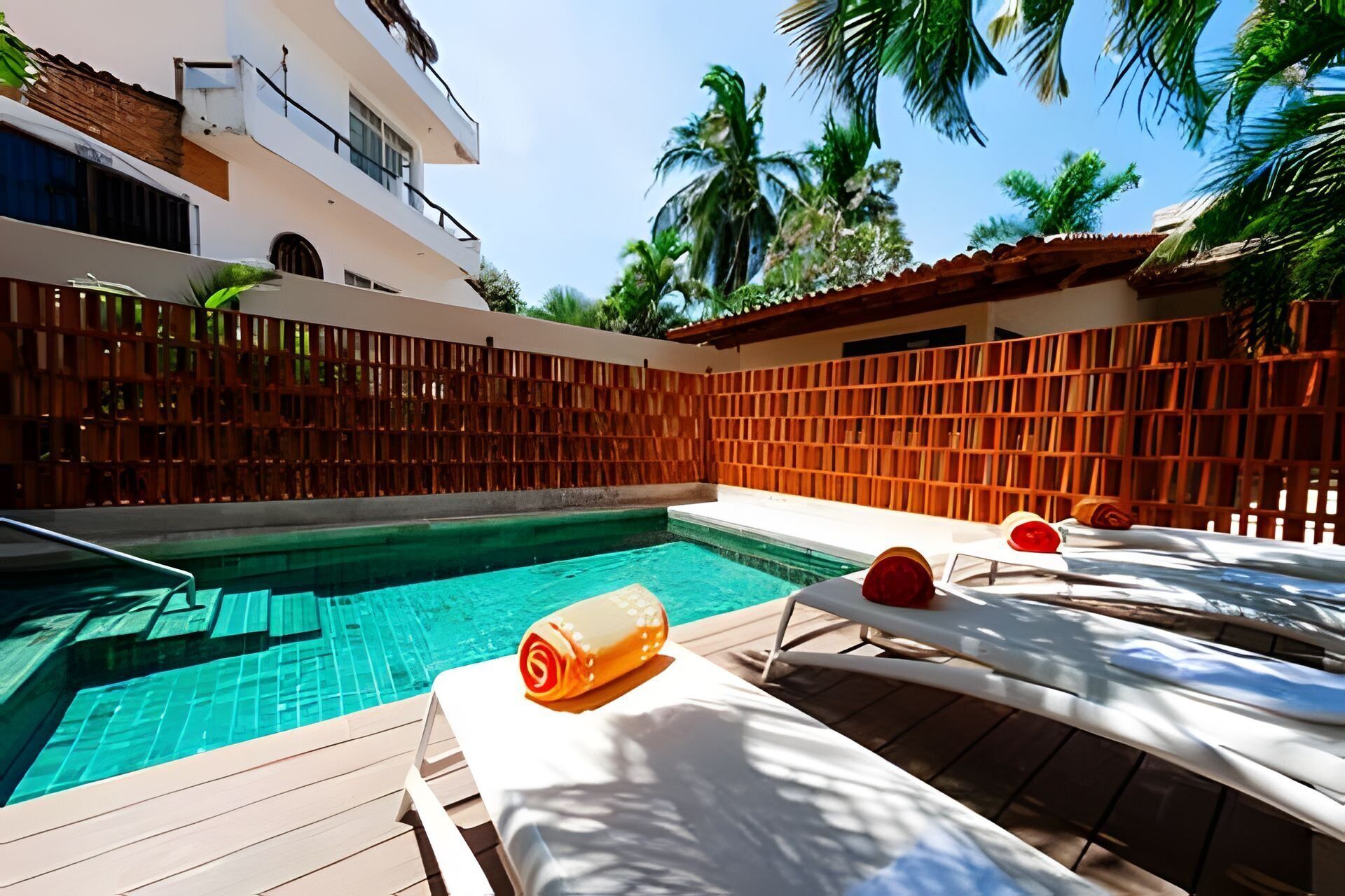 A swimming pool with a wooden deck, lounge chairs, and a wooden fence.