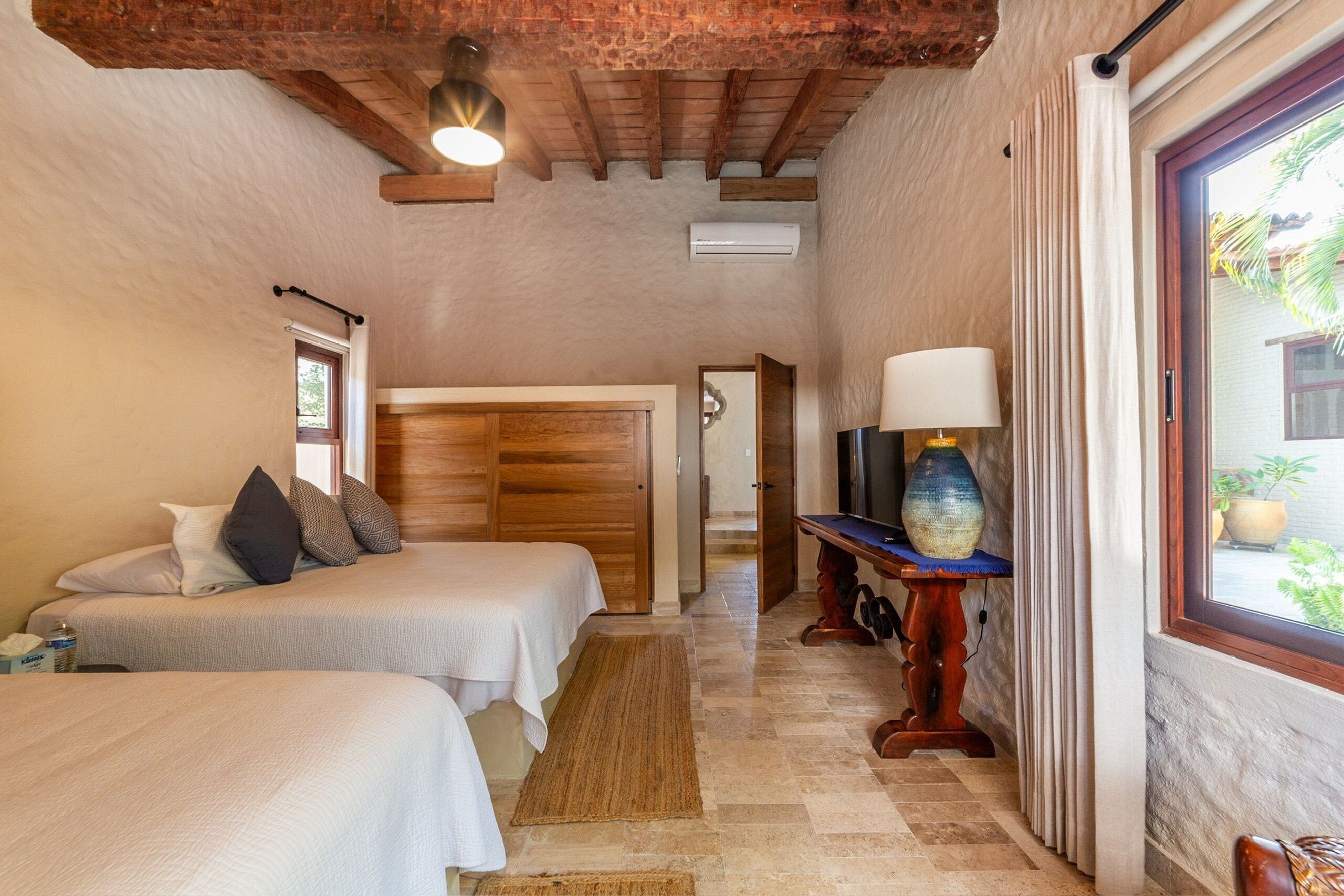 A bedroom with two beds, a wooden headboard, a TV, and a window with curtains.