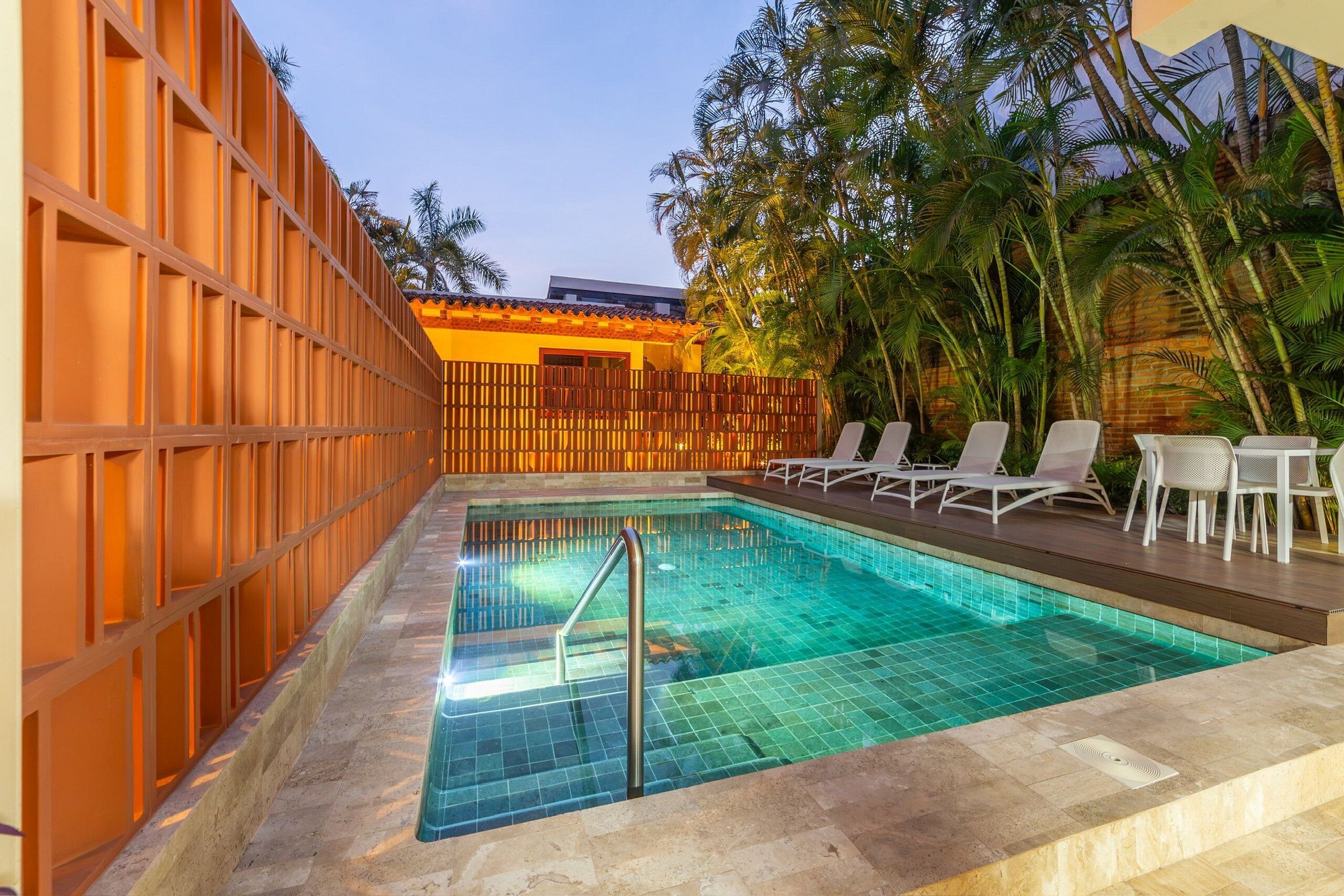 Une piscine dotée d’une terrasse carrelée, entourée d’une clôture en bois et de palmiers.