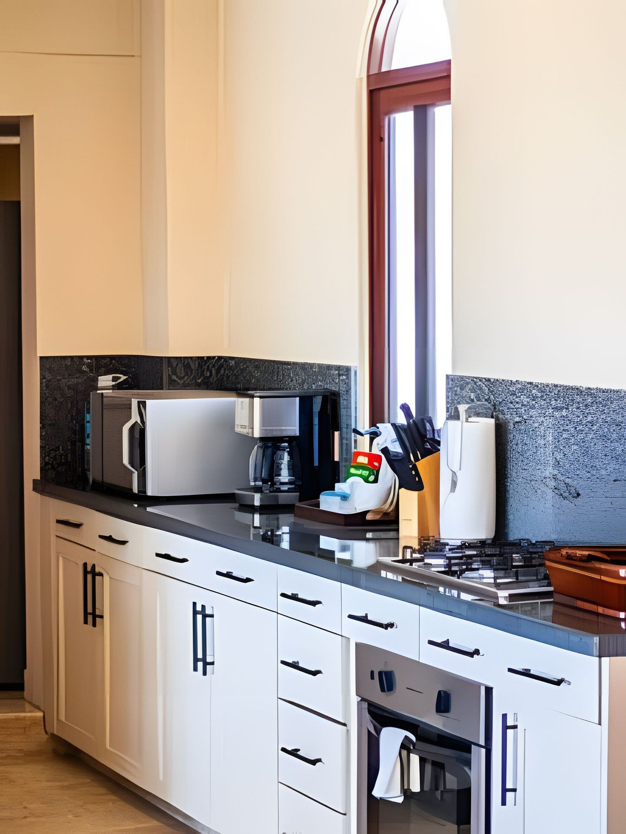 A modern kitchen with white cabinets, a black countertop, a coffee machine, and a window with a view.