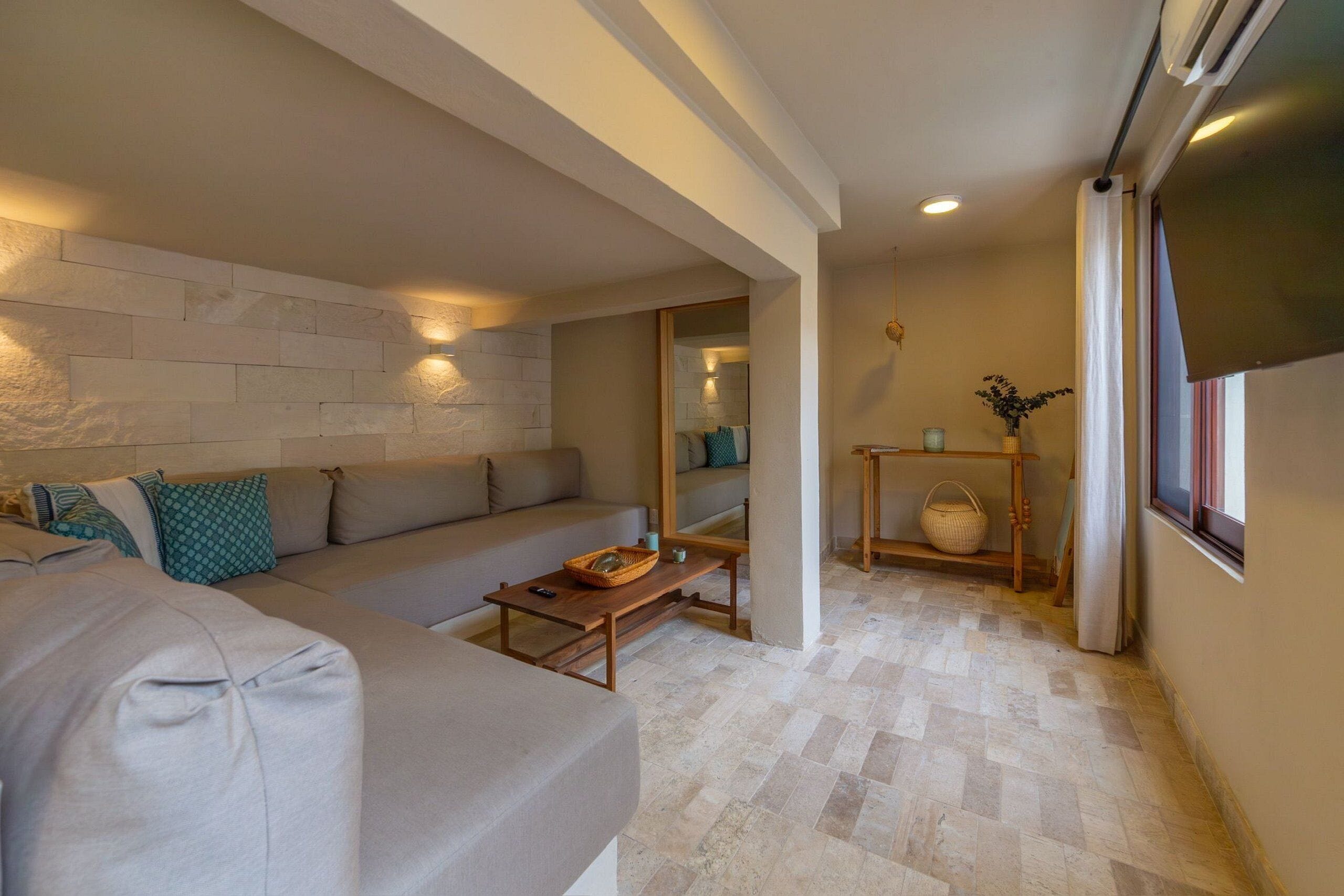 A modern living room with a grey sofa, a wooden coffee table, and a stone wall.