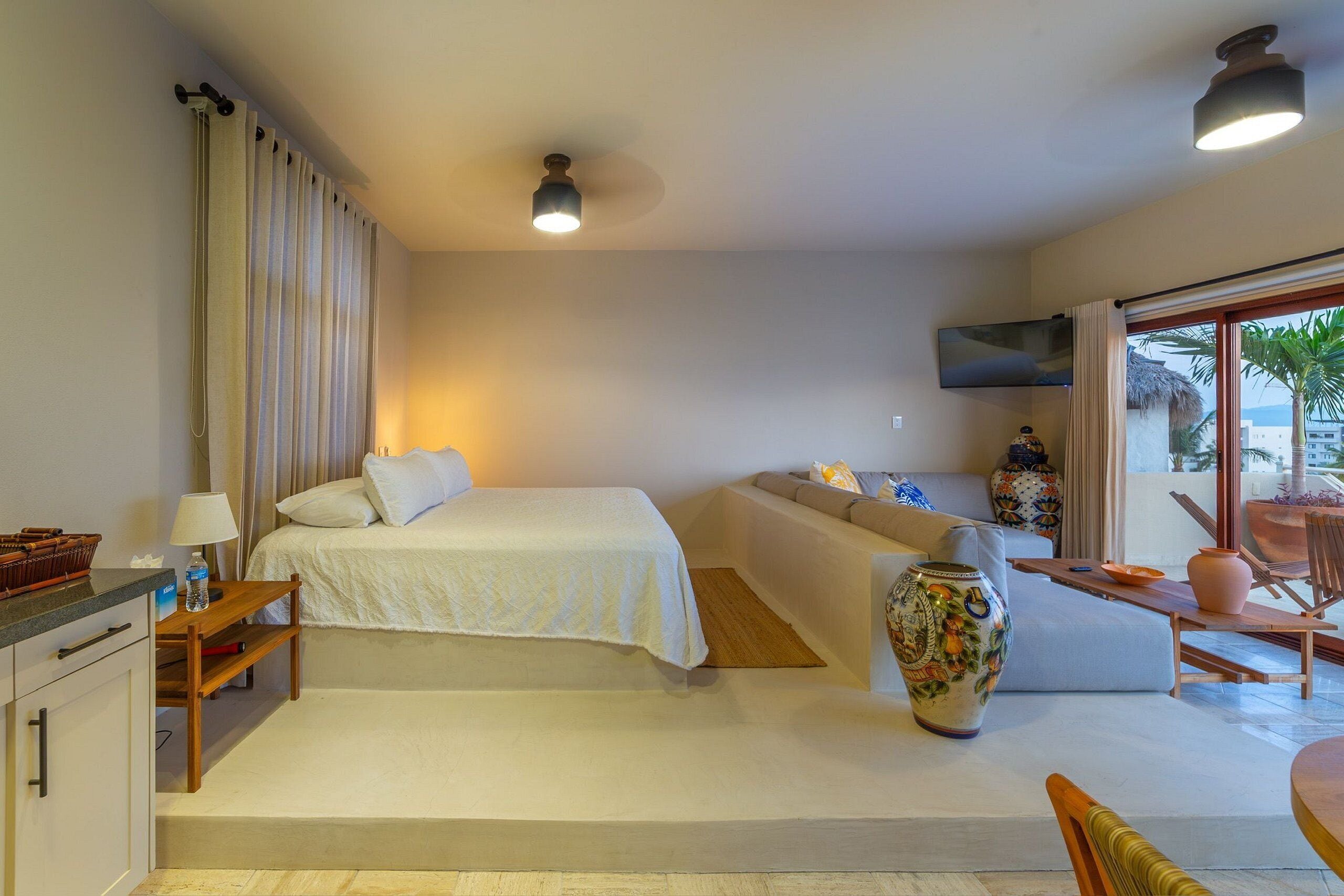 A bedroom with a bed, a sofa, a TV, a large vase, and a dining area with a table and chairs.