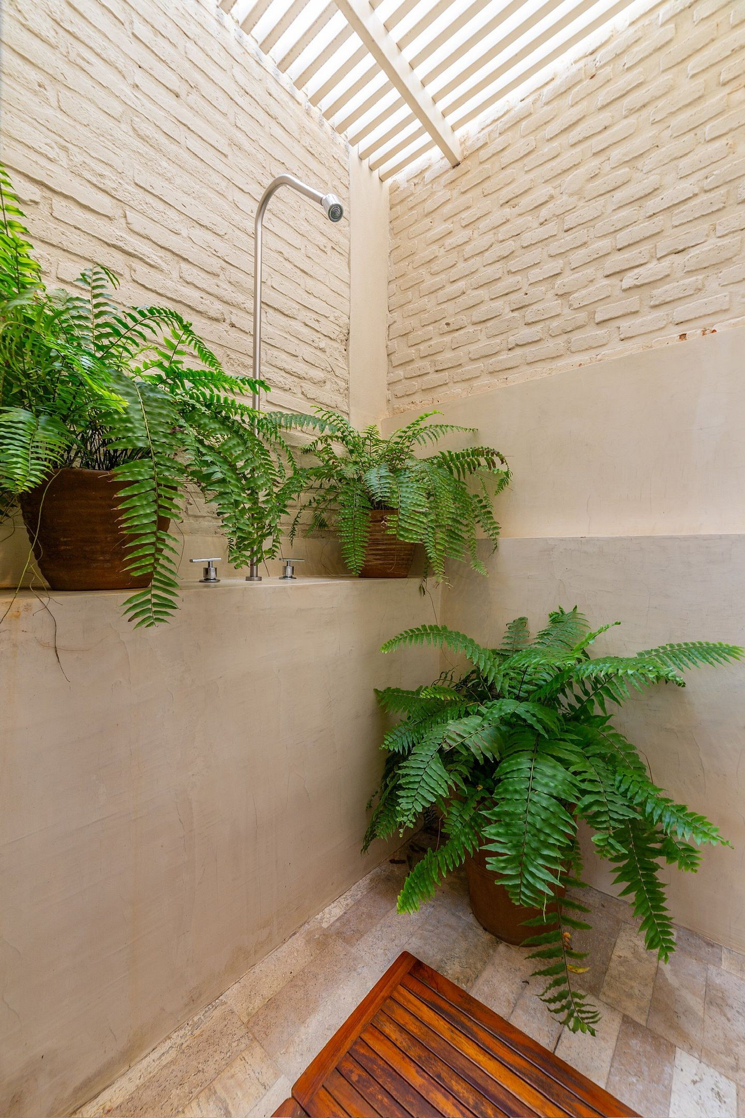 A bathroom with a brick wall, a wooden bench, and potted ferns.