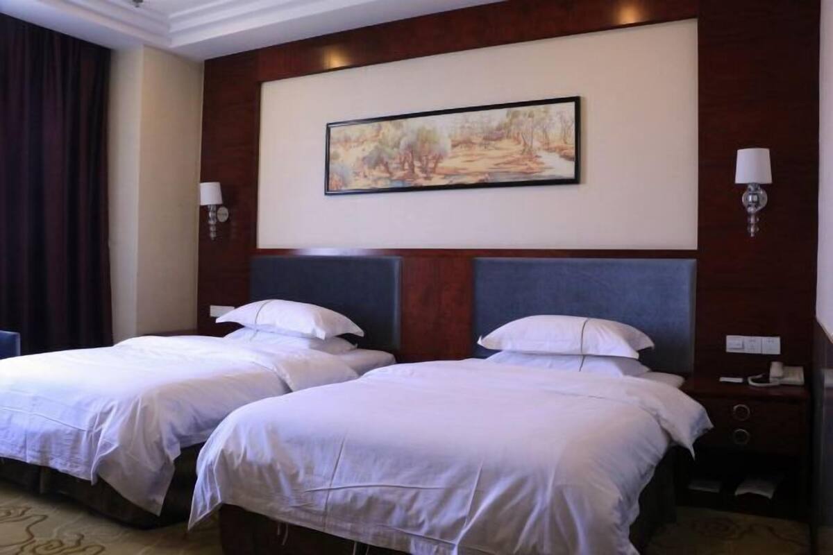 Une chambre d’hôtel avec deux lits, un tableau au mur et une table de chevet avec une lampe.