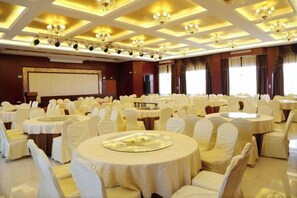 A banquet hall with round tables, white chairs, and chandeliers. - Jiangang Hotel (Qianshan)