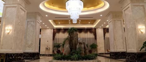 Un vestíbulo con piso de mármol, una araña y un elemento decorativo central con plantas.