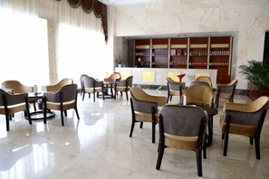 A hotel lobby with multiple seating areas, a reception desk, and a bookshelf. - Jiangang Hotel (Qianshan)