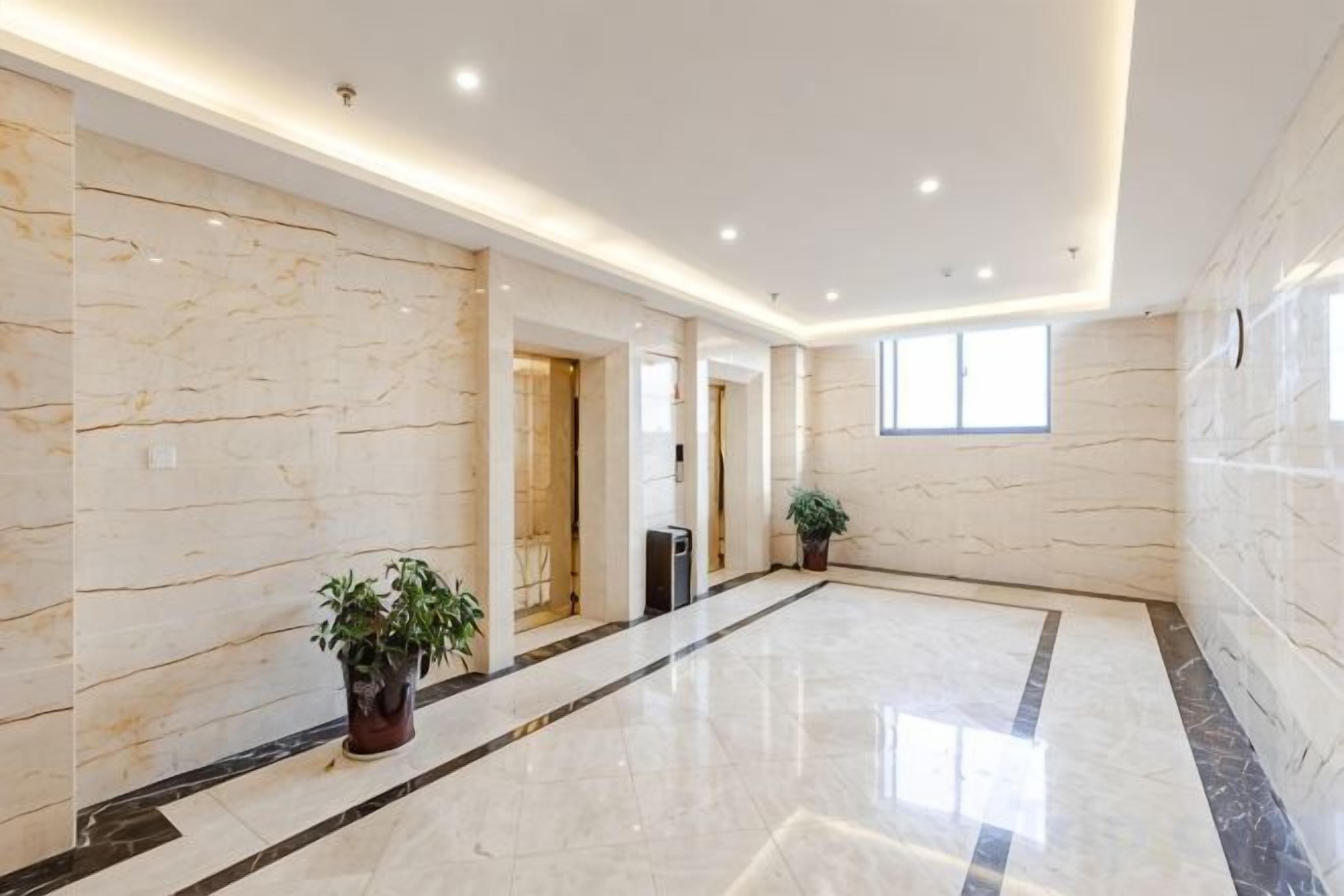 A spacious hallway with marble walls and a polished floor, leading to a door.
