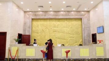 A reception area with a marble wall, a reception desk, and a digital screen.