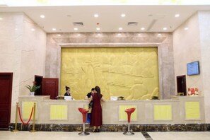 A reception area with a marble wall, a reception desk, and a digital screen. - Jiangang Hotel (Qianshan)
