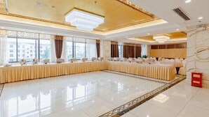 Une grande salle de banquet, bien éclairée, avec une longue table, de grandes fenêtres et un plafond décoratif.