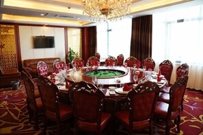 A conference room with a round table, red upholstered chairs, a chandelier, and a television on the wall. - Jiangang Hotel (Qianshan)