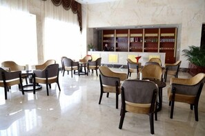 A hotel lobby with multiple seating areas, a reception desk, and a bookshelf. - Jiangang Hotel (Qianshan)