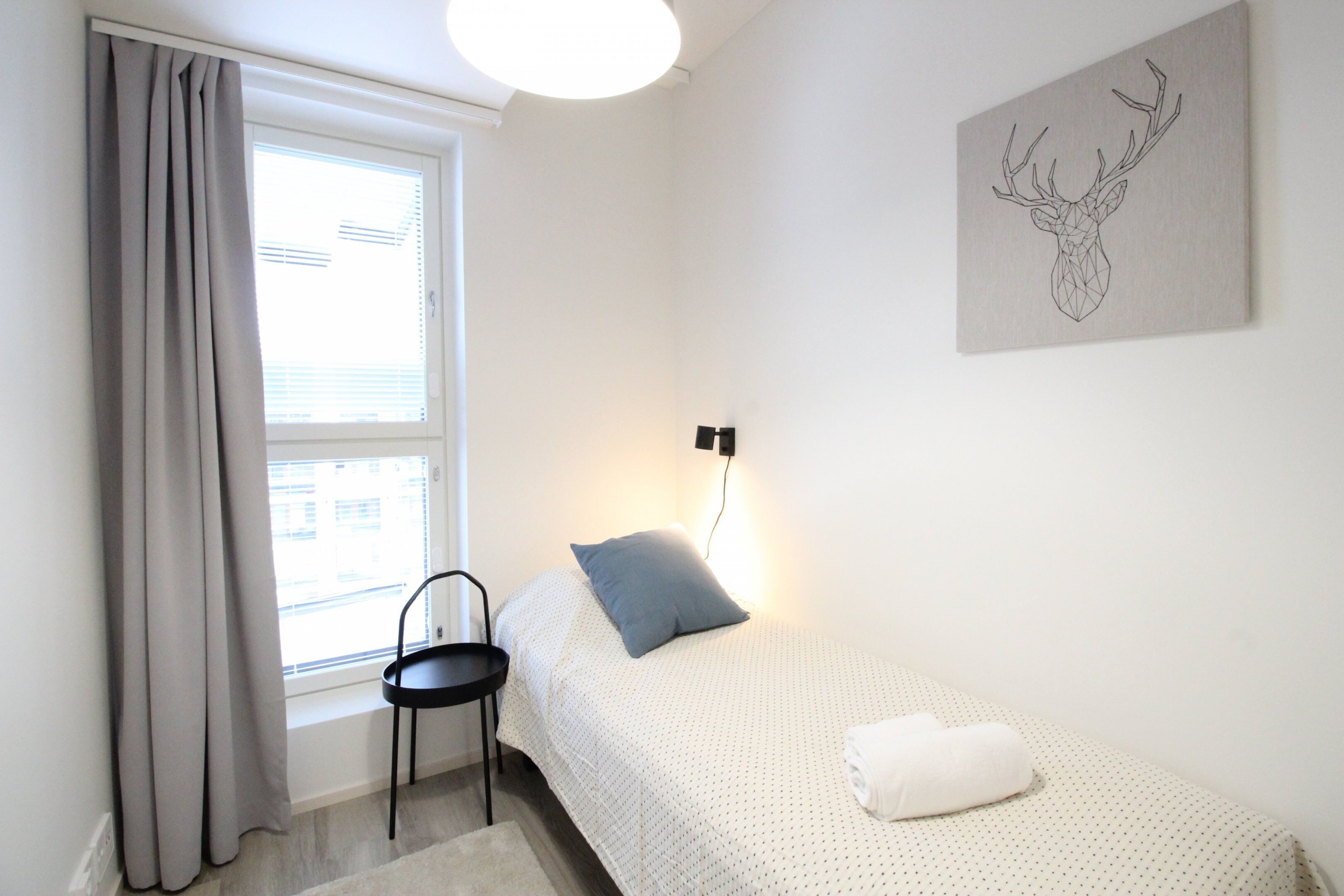 Una camera da letto con un letto, una sedia, una finestra con tende e una lampada a parete.