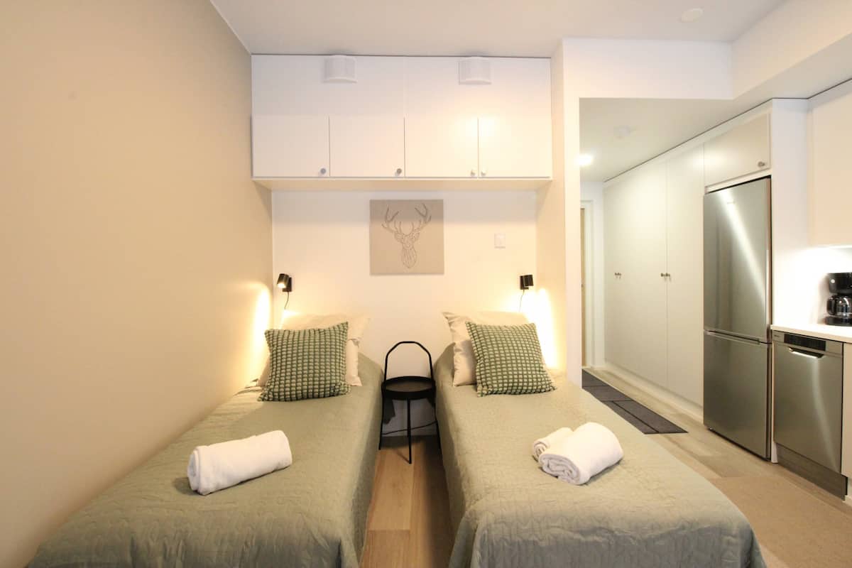 Una habitación pequeña y luminosa con dos camas, una kitchenette y un ventilador de techo.