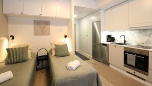 A modern hotel room with two beds, a kitchenette, and a bathroom.