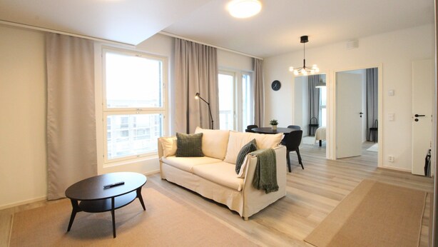 A modern living room with a sofa, a coffee table, and a dining area in the background.